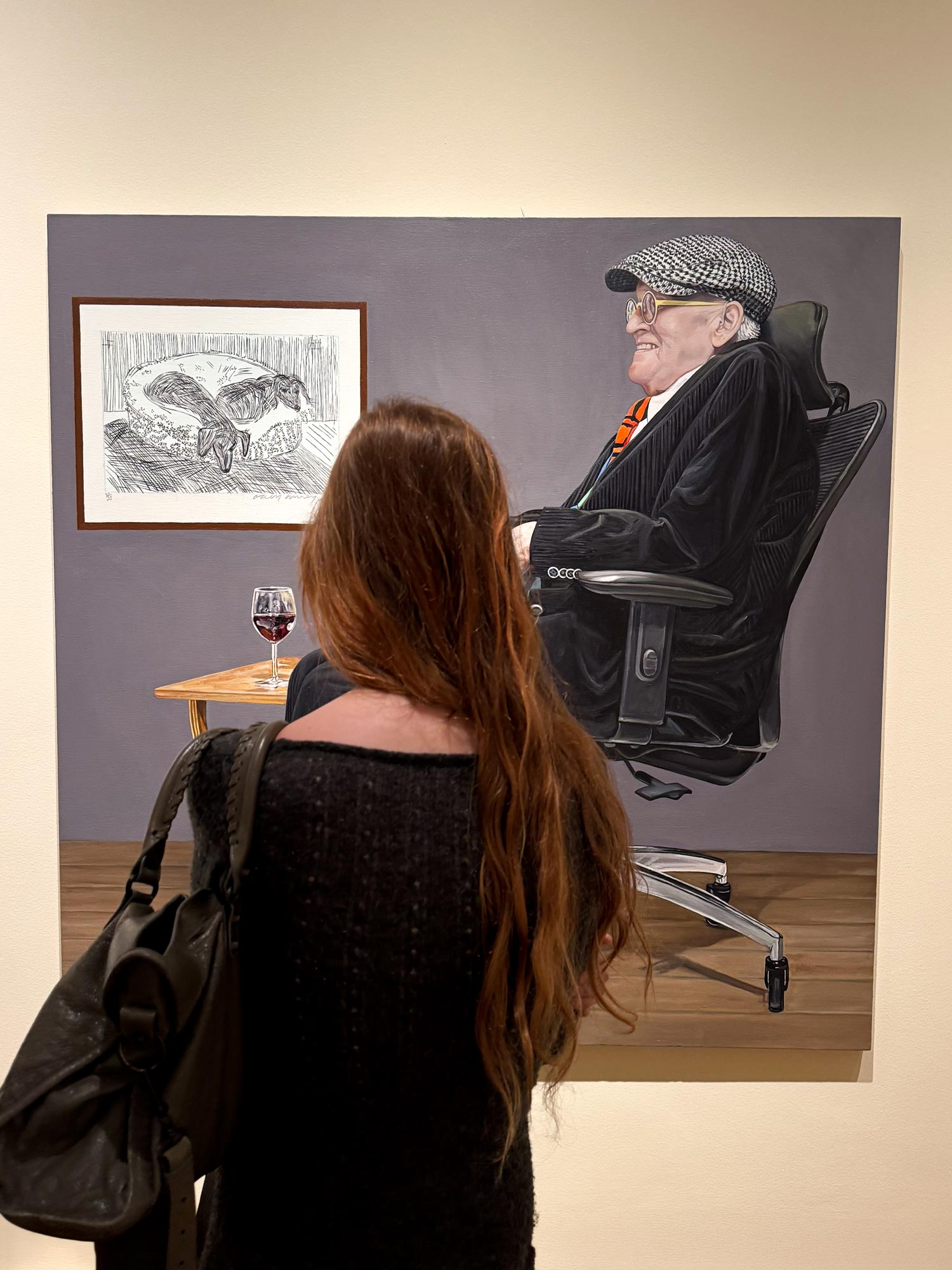 An image of a woman looking at a portrait of David Hockney